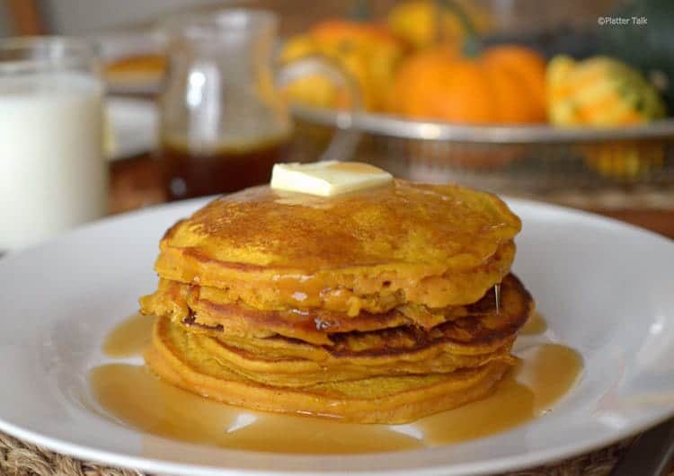 Stack of pumpkin pancakes with butter and syrup on a white plate.