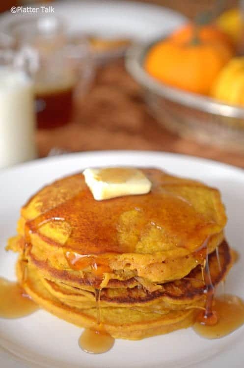 Stack of Pumpkin Pancakes on a white plate with butter and dripping syrup.