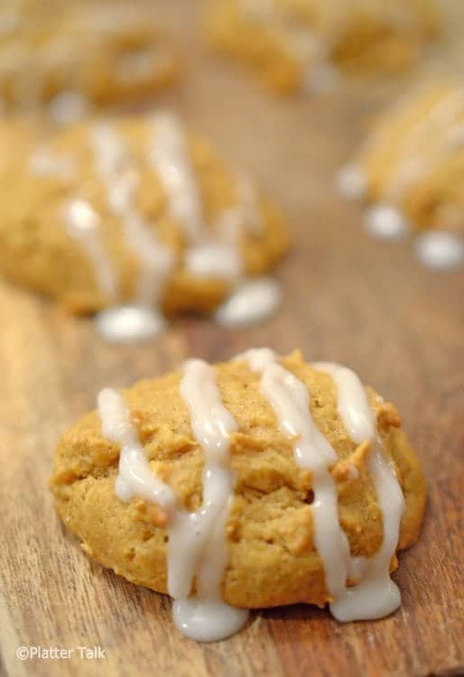 Pumpkin cookies with oozy vanilla frosting on cutting board.