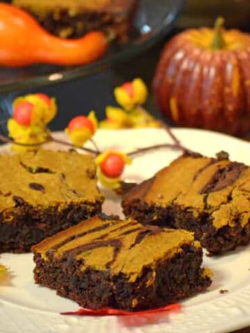 A plate of brownies with a pumpkin in the background.