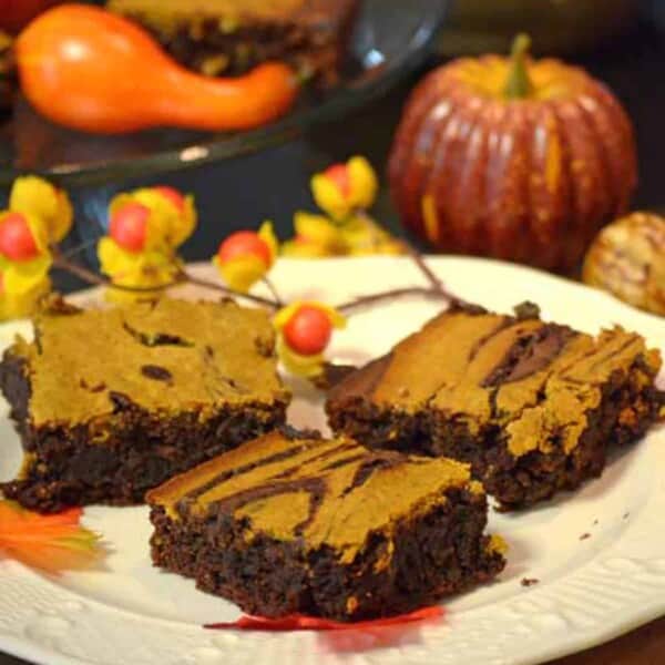 A plate of brownies with a pumpkin in the background.