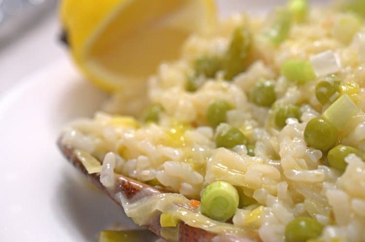Risotto plated with peas and diced vegetable with cut lemon background
