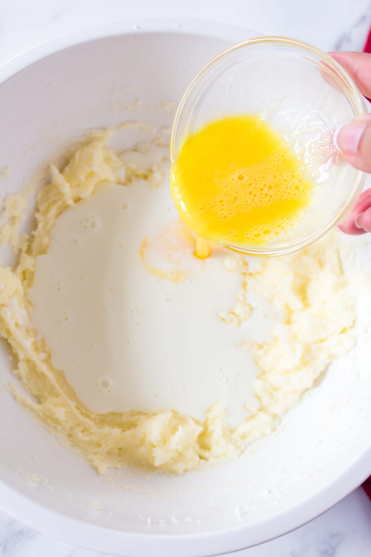 Adding a beaten egg to a mixing bowl full of dough.
