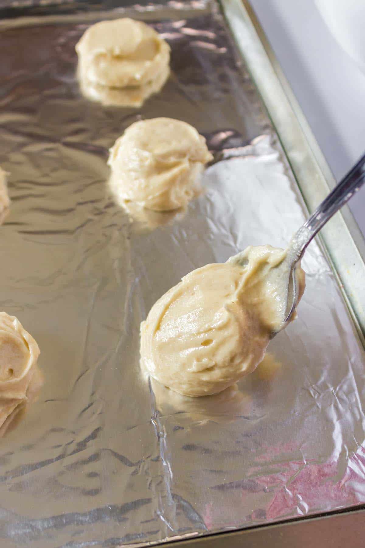 Some cookie dough being dropped onto a baking sheet line with foil.