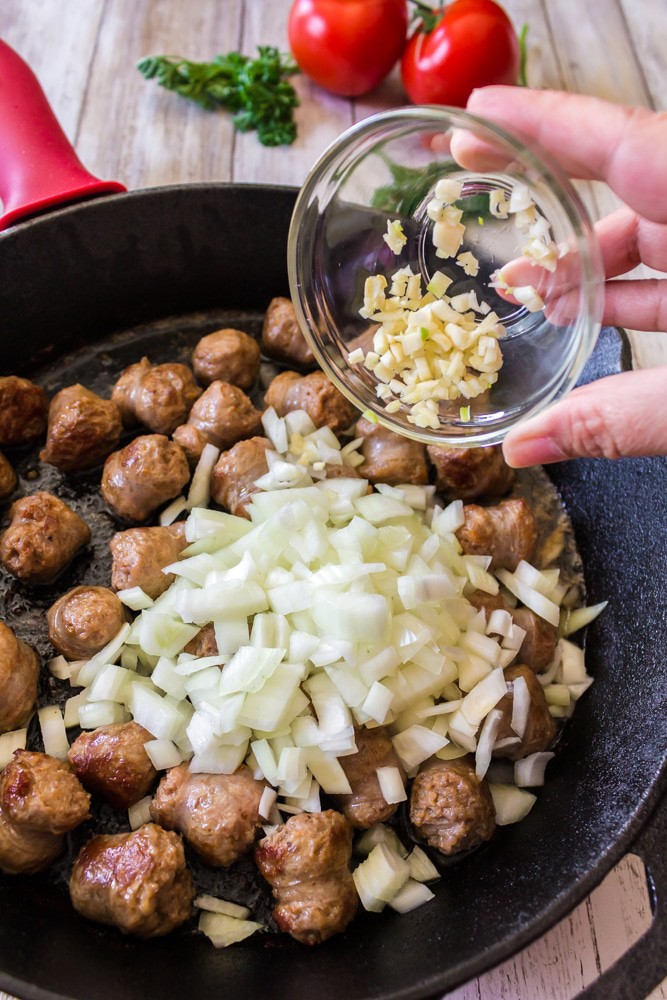 Adding chopped garlet to a skillet of sausge and onion.