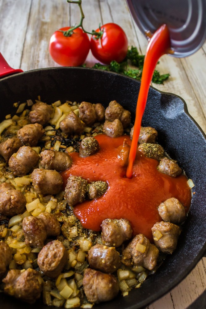 Tomoato sauce being added to a skillet of browned sausage.