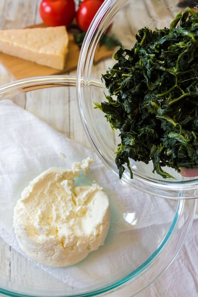 Spinach being added to a bowl of ricotta cheese.