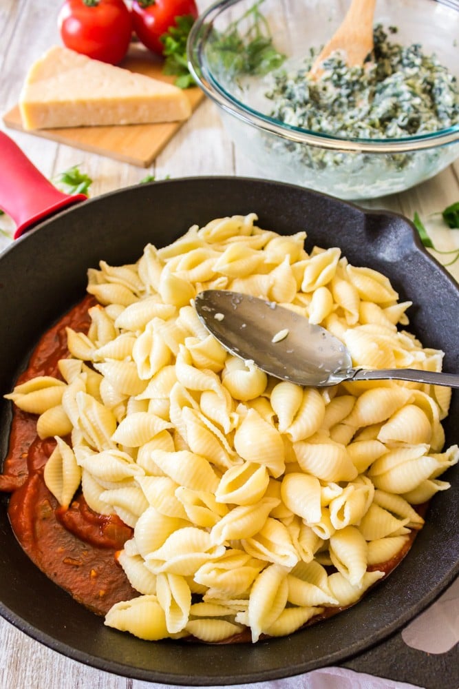 Shell pasta in a skillet with bowl of lasagna ingredients.