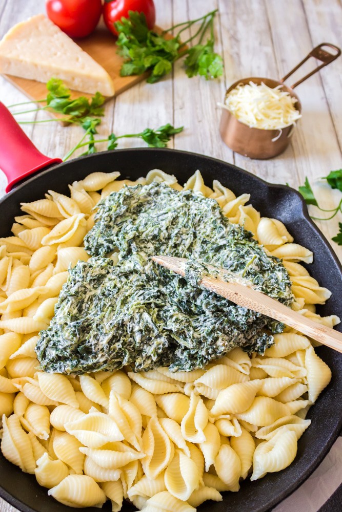 spreadking cheese and spinach on top of cooked pasta in skillet.