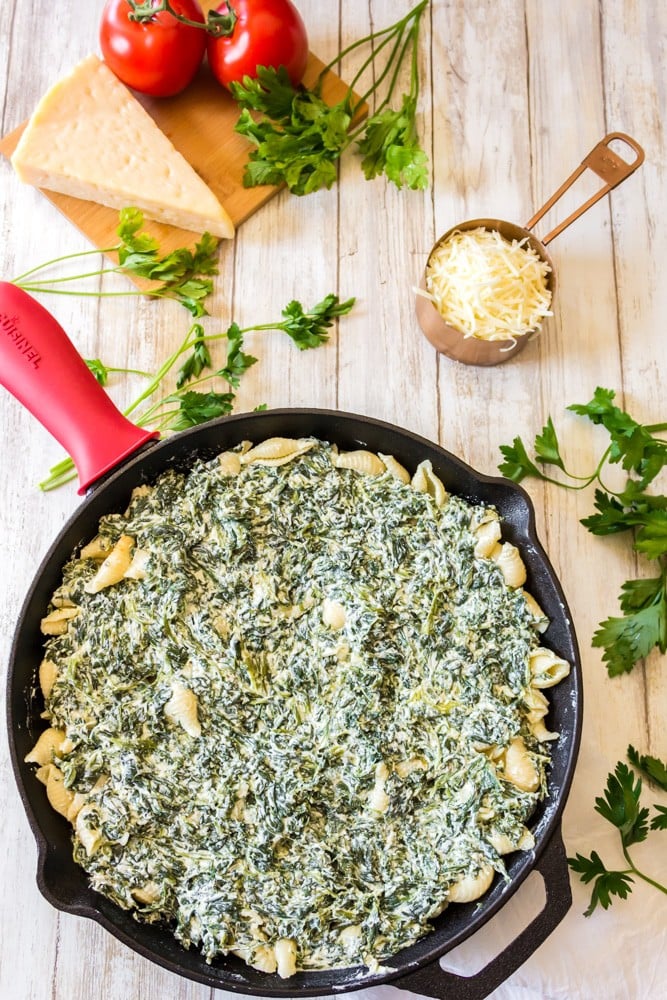 Skillet of pasta covered with ricotta cheese and spinach.