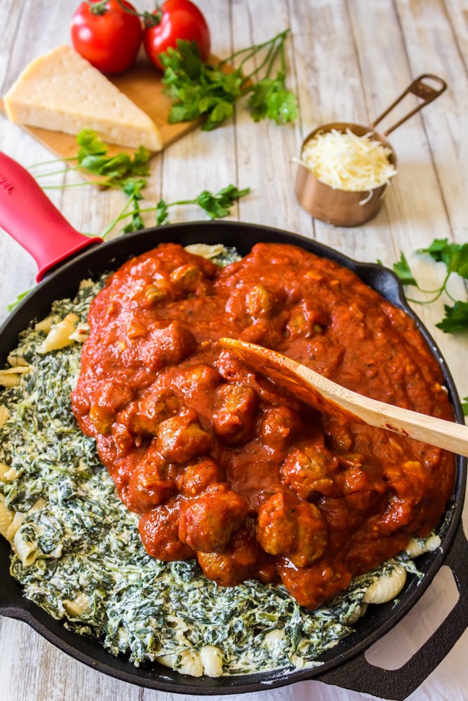 Spreading lasagna sauce on cheese and spinach layer.