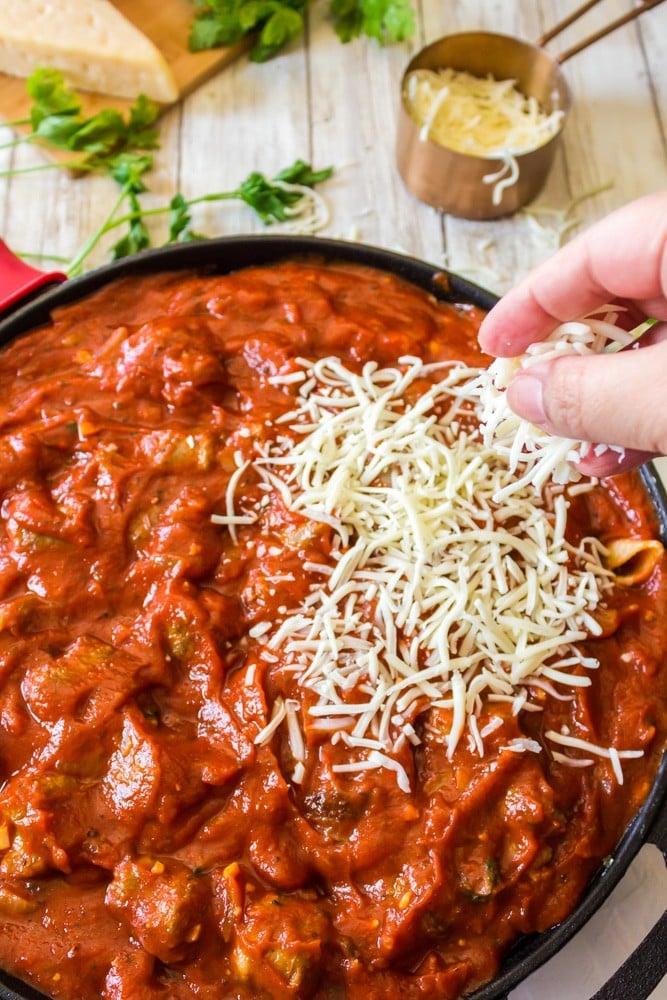 Adding Parmesan cheese on top of skillet lasagna.