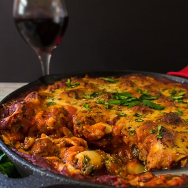 A skillet full of lasagna with a glass of red wine