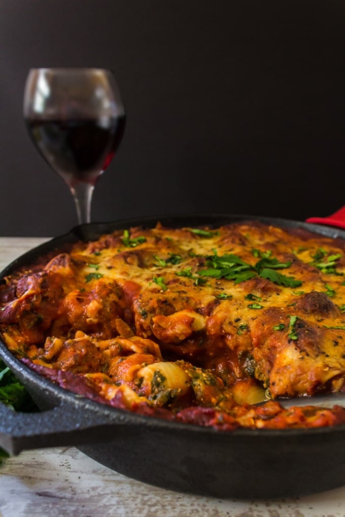 A skillet full of lasagna with a glass of red wine