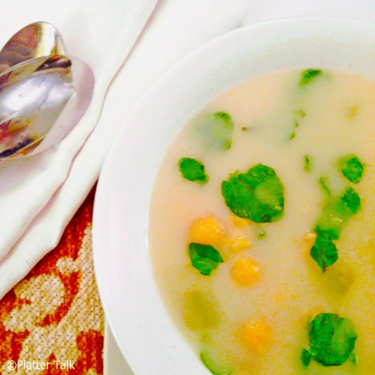 two spoons on a napkin with a bowl of vegetable soup garnished with watercress