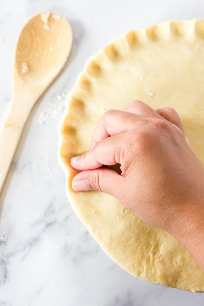 Using fingers to crimp the top of a homemade pie crust.