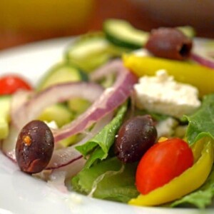 A plate of food on a table, with Greek salad.