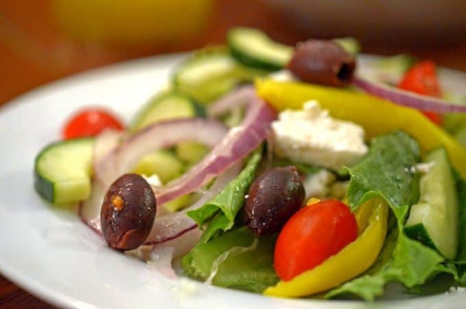 A plate of food on a table, with Greek salad.