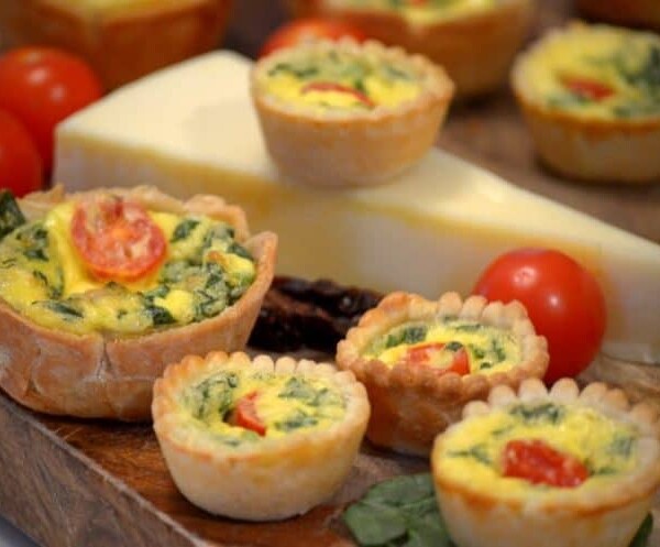 a bunch of mini quiche on a block of cheese.