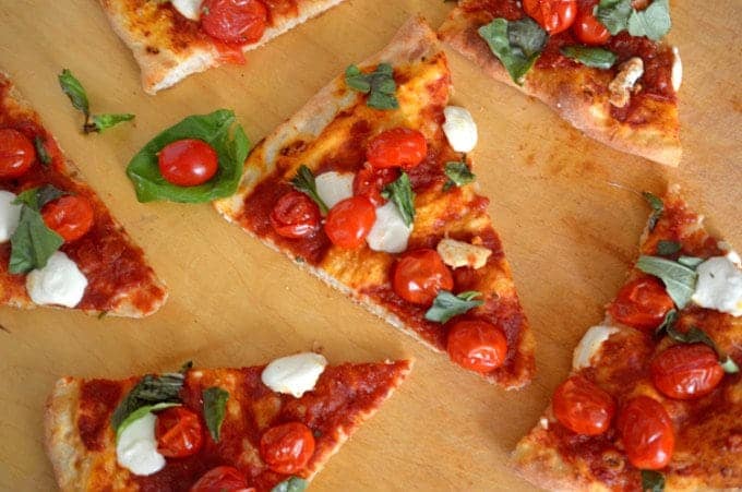 A slice of pizza sitting on top of a wooden cutting board, with Tomato and cheese.