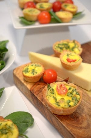 A bunch of food on a table, with Quiche and cheese.
