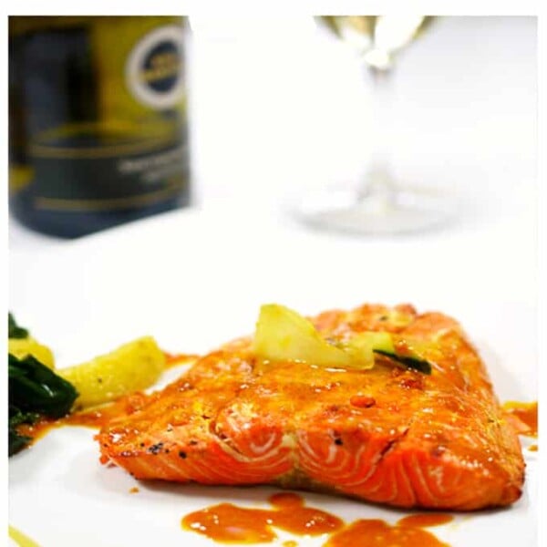 A serving of salmon on a white plate and a glass of white wine