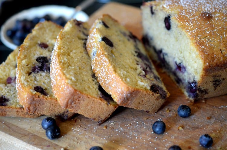 Sliced blueberry bread on a cutting board with loose blueberries.