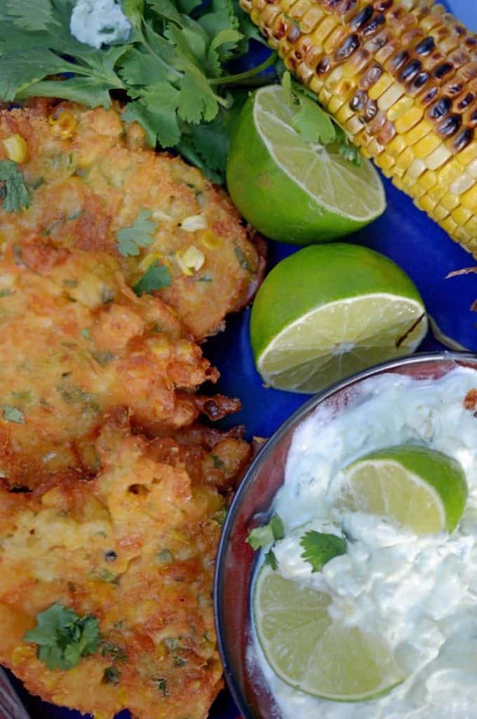 Plate of fresh corn fritters with lime wedges and grilled corn on the cob.