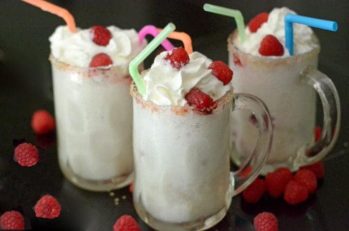 Three ice cream floats in mugs with straws and whipped cream and berries.