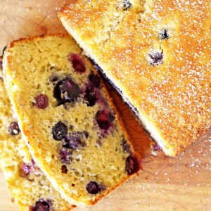 Loaf of blueberry bread with two slices on a cutting board.