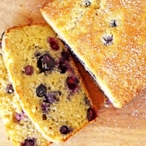 Loaf of blueberry bread with two slices on a cutting board.