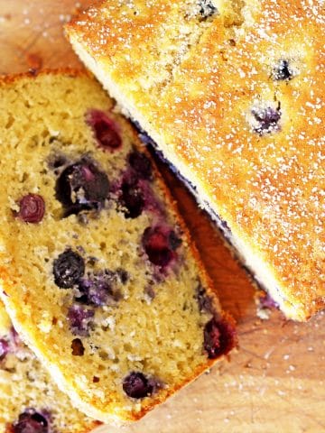 Loaf of blueberry bread with two slices on a cutting board.