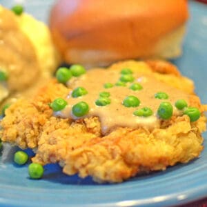 A piece of meat with gravy and peas.