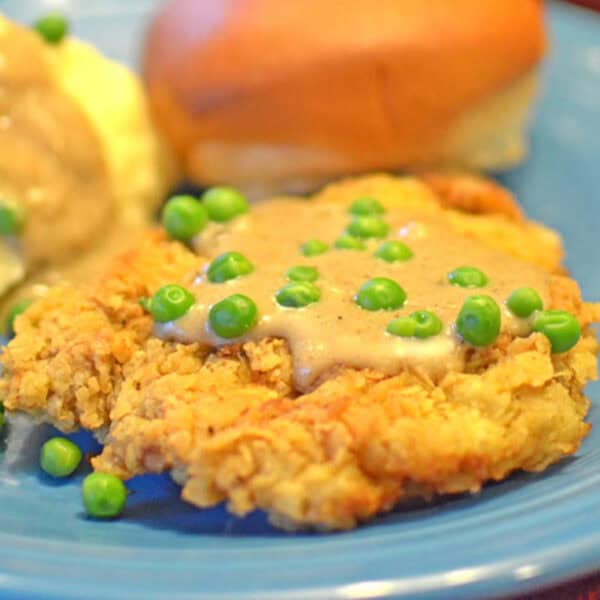 A piece of meat with gravy and peas.