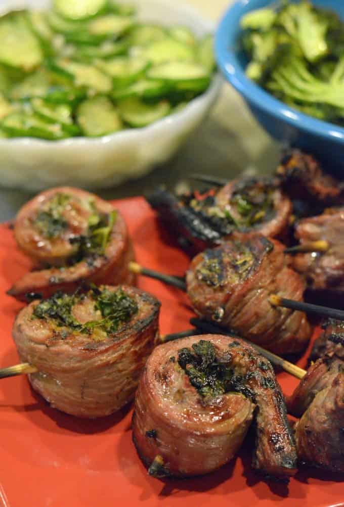 Serving platter of flank steak pinwheels with salad in the background.