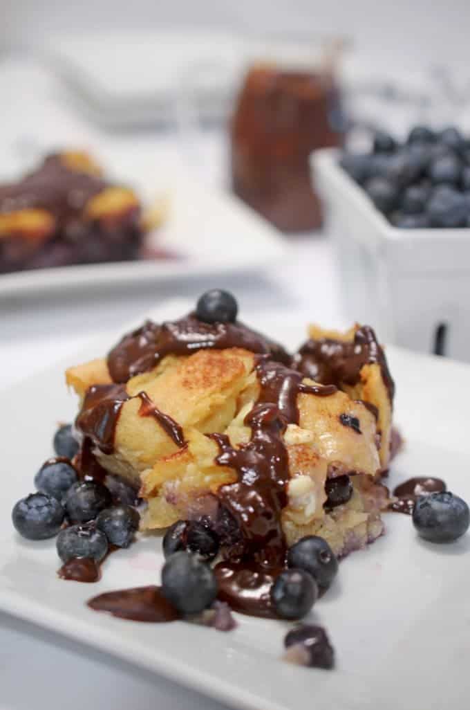 A piece of bread pudding on a plate with blueberries.