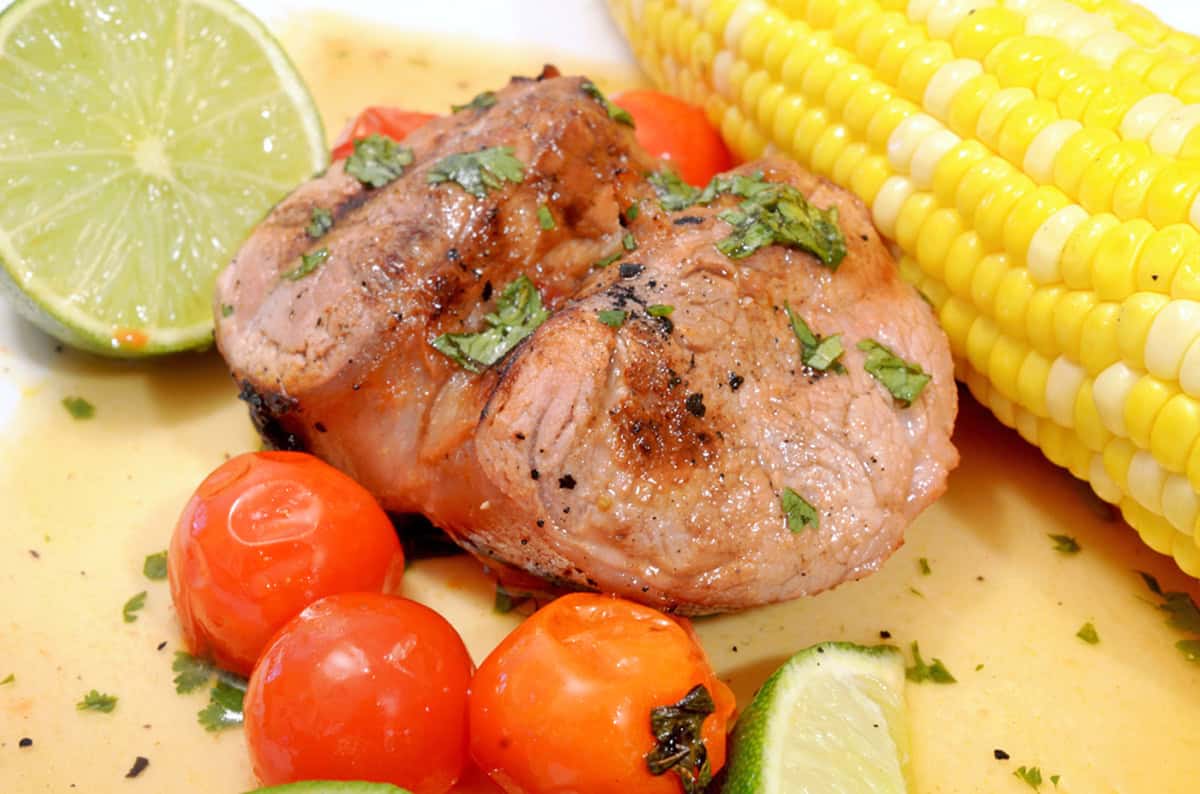 A serving of pork chop on a plate with corn on the cob.