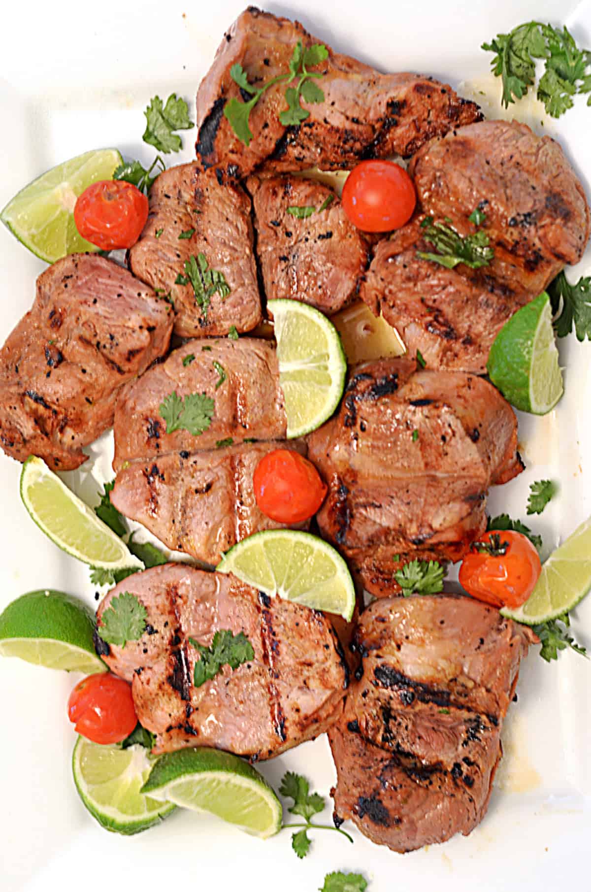 A platter of grilled pork loin garnished with lime and cilantro.