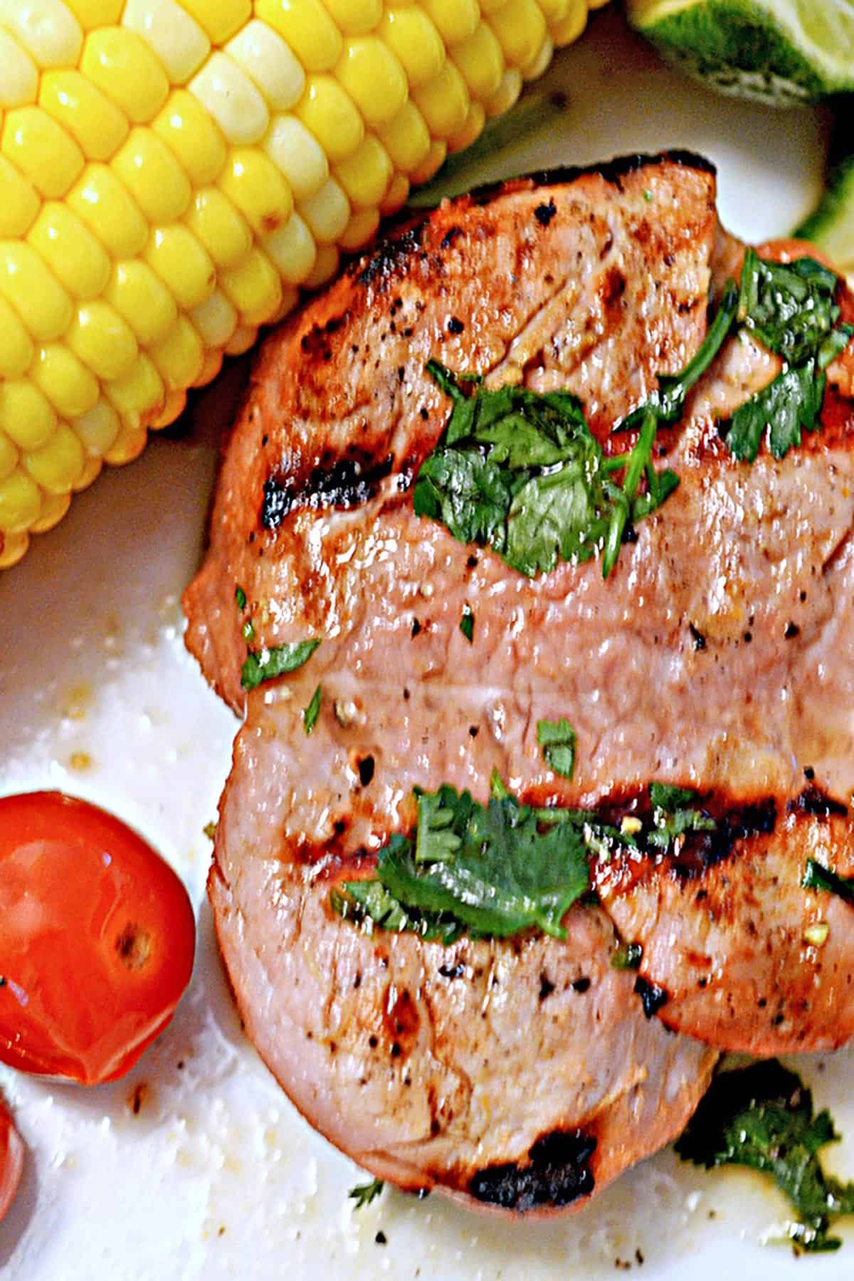 Close up of a grill pork chop with corn on the cob.