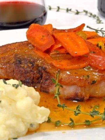 A plate with a pork chop and glazed carrots.
