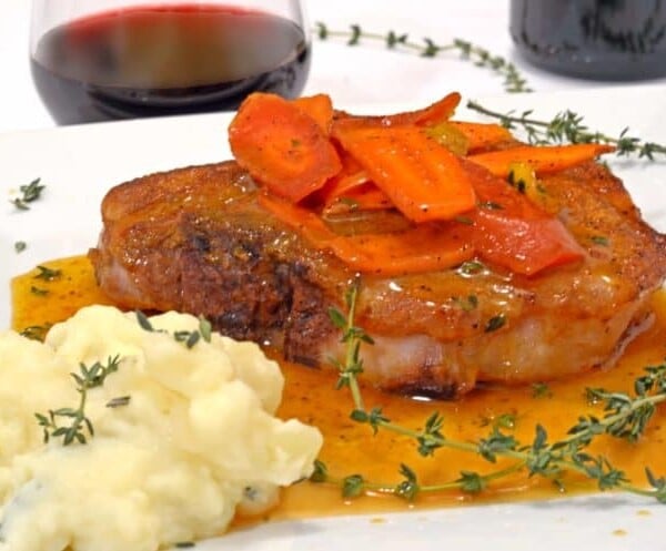 A plate with a pork chop and glazed carrots.