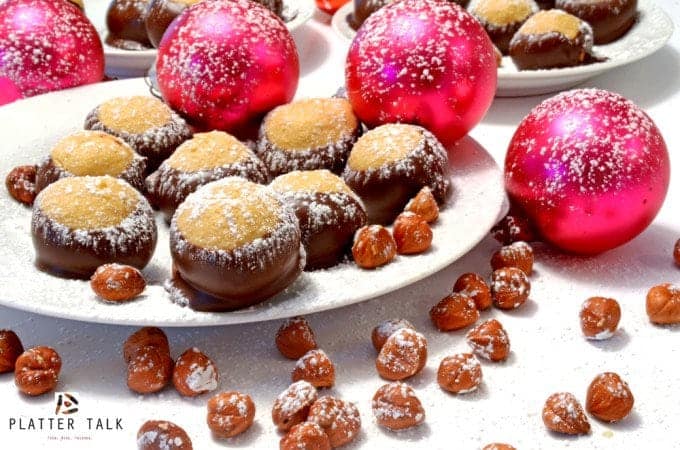 Plate of holiday treats with ornaments and hazelnuts, dusted with powedered sugar.