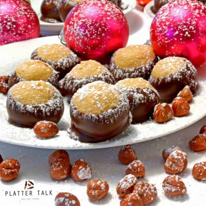 Festive plate of buckeye candies with hazelnuts and ornaments dusted with powdered sugar.
