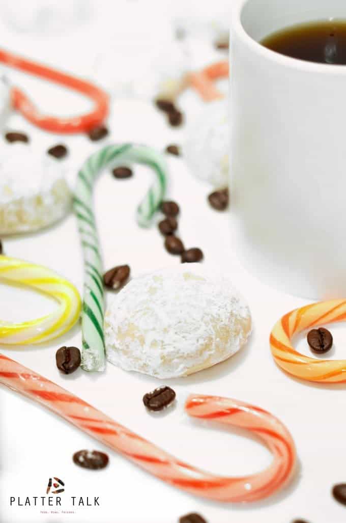 White mug of coffee surrounded by snowball cookies and candy canes.