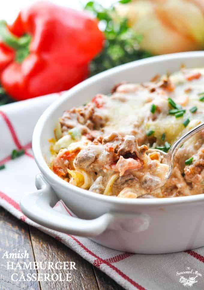 Someone spooning out casserole of food on table, red pepper in background