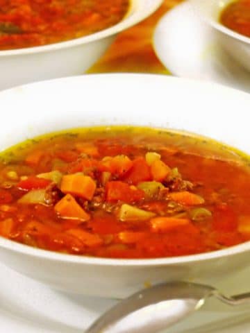 White bowl of ground beef soup with a spoon.