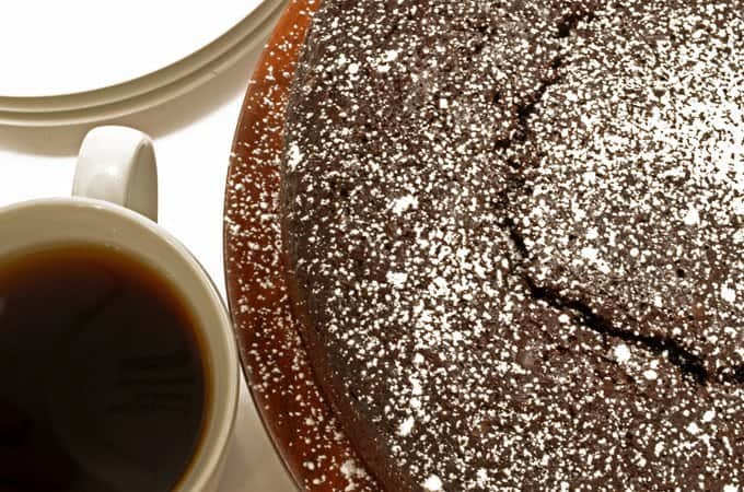 The top view of a chocolate cake dusted in powdered sugar and a cup of coffee.