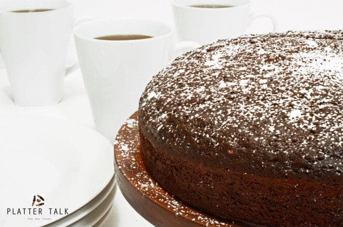 Homemade chocolate cake with three cups of coffee in the background.