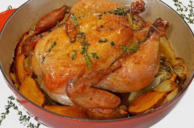 a whole chicken with herbs in a pan.