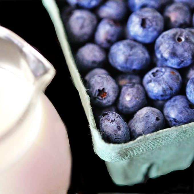 Baskedt of fresh blueverries and a pitcher of half & half cream.